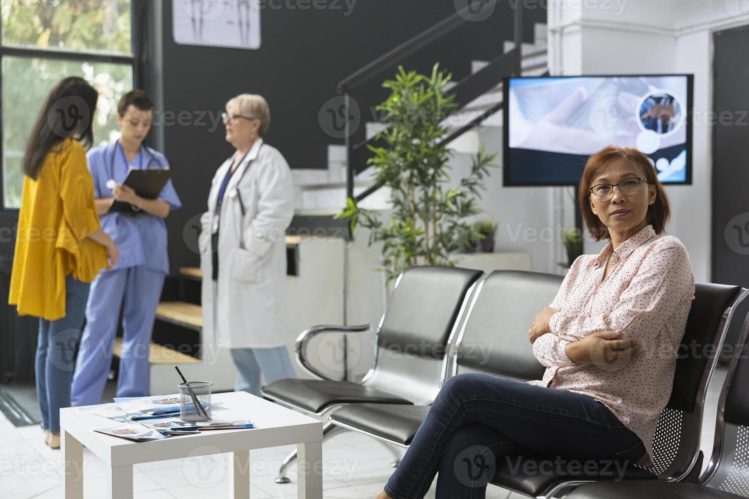 Asian woman sitting in hospital lobby and waiting for routine checkup, having an appointment with general practitioner. Enjoying public health service for wellness and prevention. photo