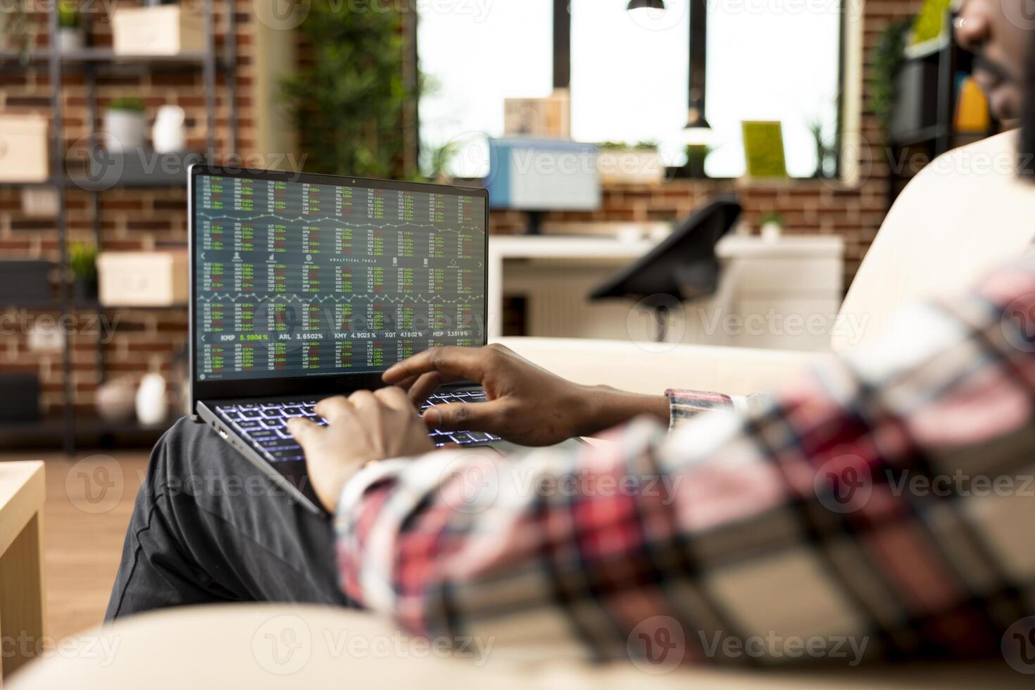 African american businessman focused on laptop screen, analyzing financial charts and stock indexes. Black male entrepreneur checking investment data for cryptocurrency market trends. photo