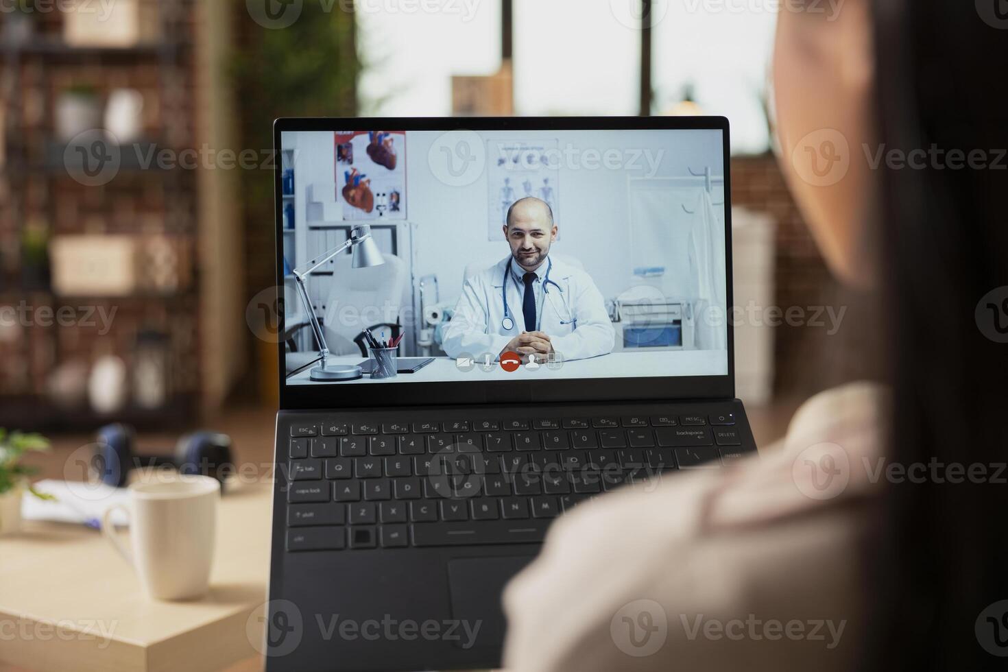 Back view of woman making call with caucasian male doctor from home. Close up of female patient using laptop for remote consultation with general practitioner through telehealth service. photo