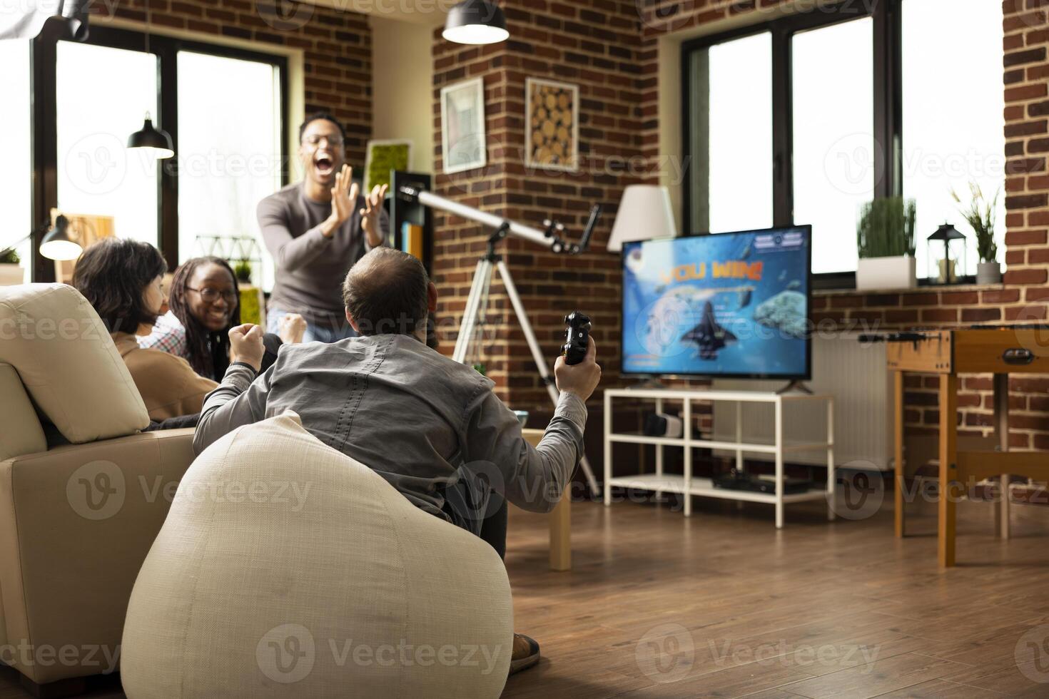 Multiracial friends rejoice after winning space simulation game on modern gaming console, gathered on sofa in living room. Laughter and celebration filled in brick wall lounge during hangout. photo