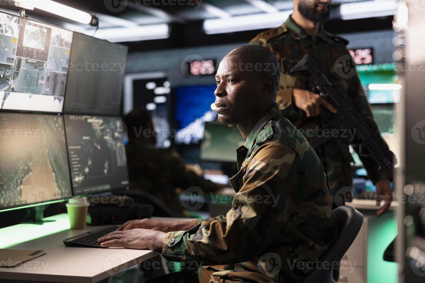 Army unit working in governmental facility operating as surveillance monitoring center filled with digital equipment. African american man doing job in base of operations photo