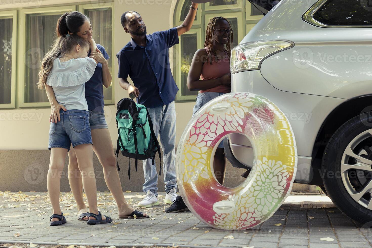 African American couple leaving on vacation with a friend and her child, preparing for a fun summer road trip. Diverse group packing the vehicle with luggage and beach essentials. Happy travel. photo