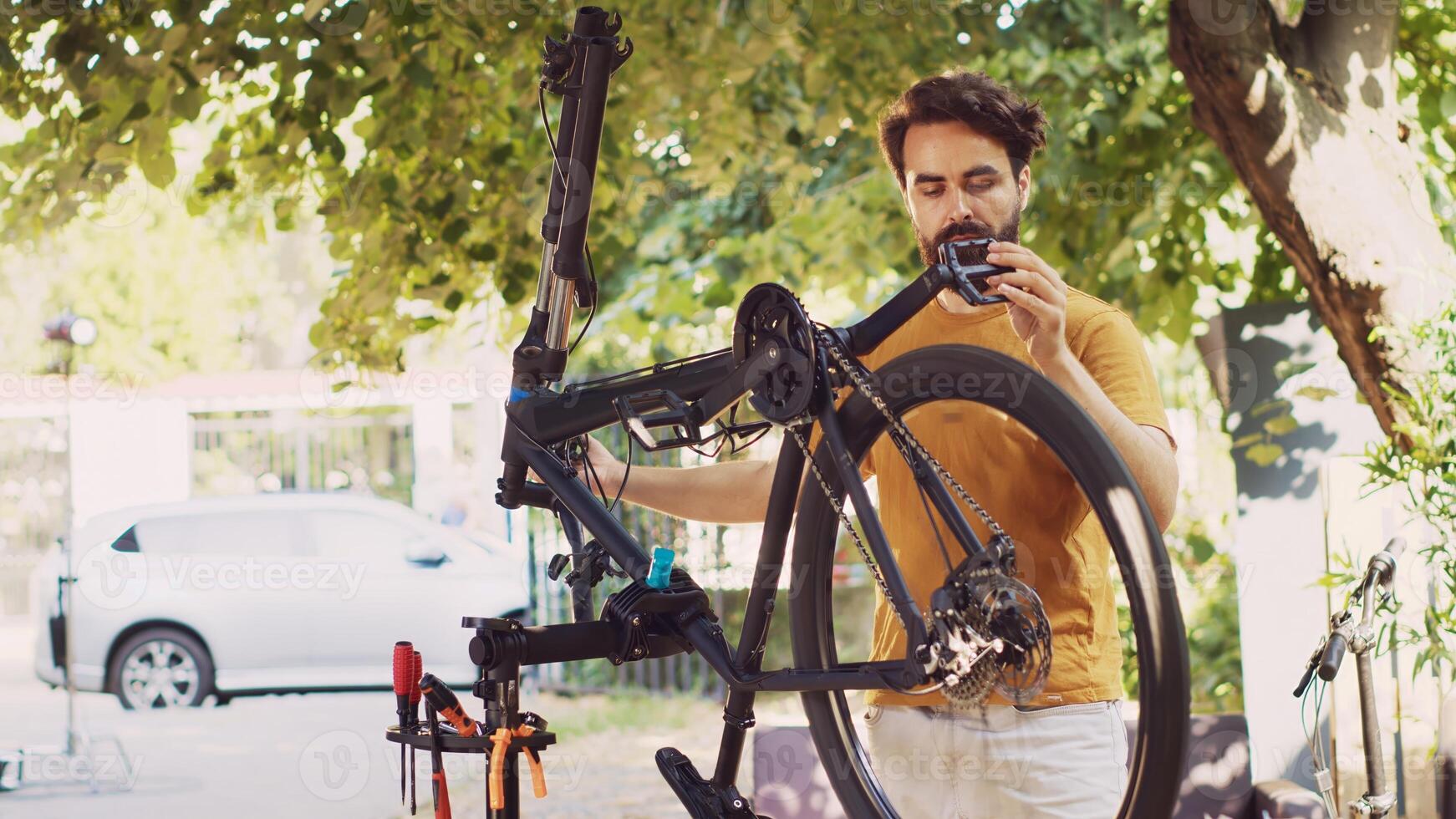 Young determined man checking bicycle parts in yard for damage that can be fixed with specialized tools. Male cyclist fixing damaged bike gear and chain outside for summertime pleasure cycling. photo