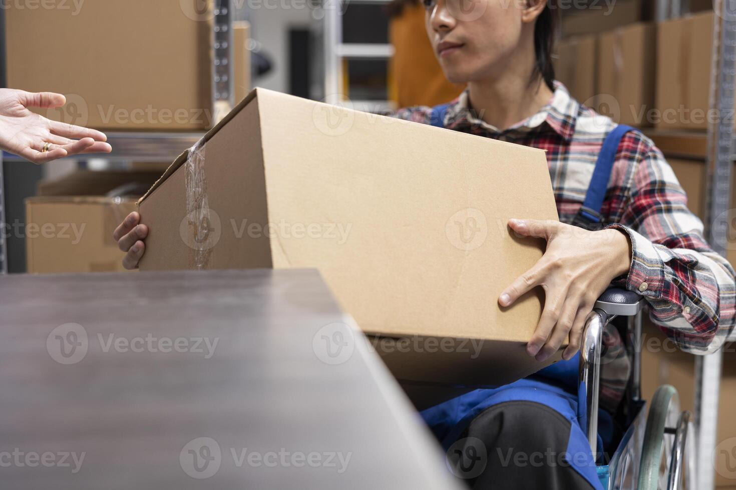Asian depot employee in wheelchair works at the packaging station with multiple boxes, preparing the orders to be shipped for local clients. Disability friendly startup space. Close up. photo