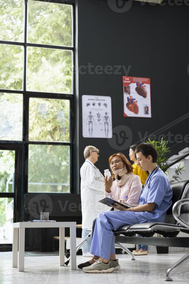 Medical assistant and asian woman discuss treatment plan and solutions for healing process after fracture. Hospital staff offering support with physiotherapy and painkillers during recovery. photo