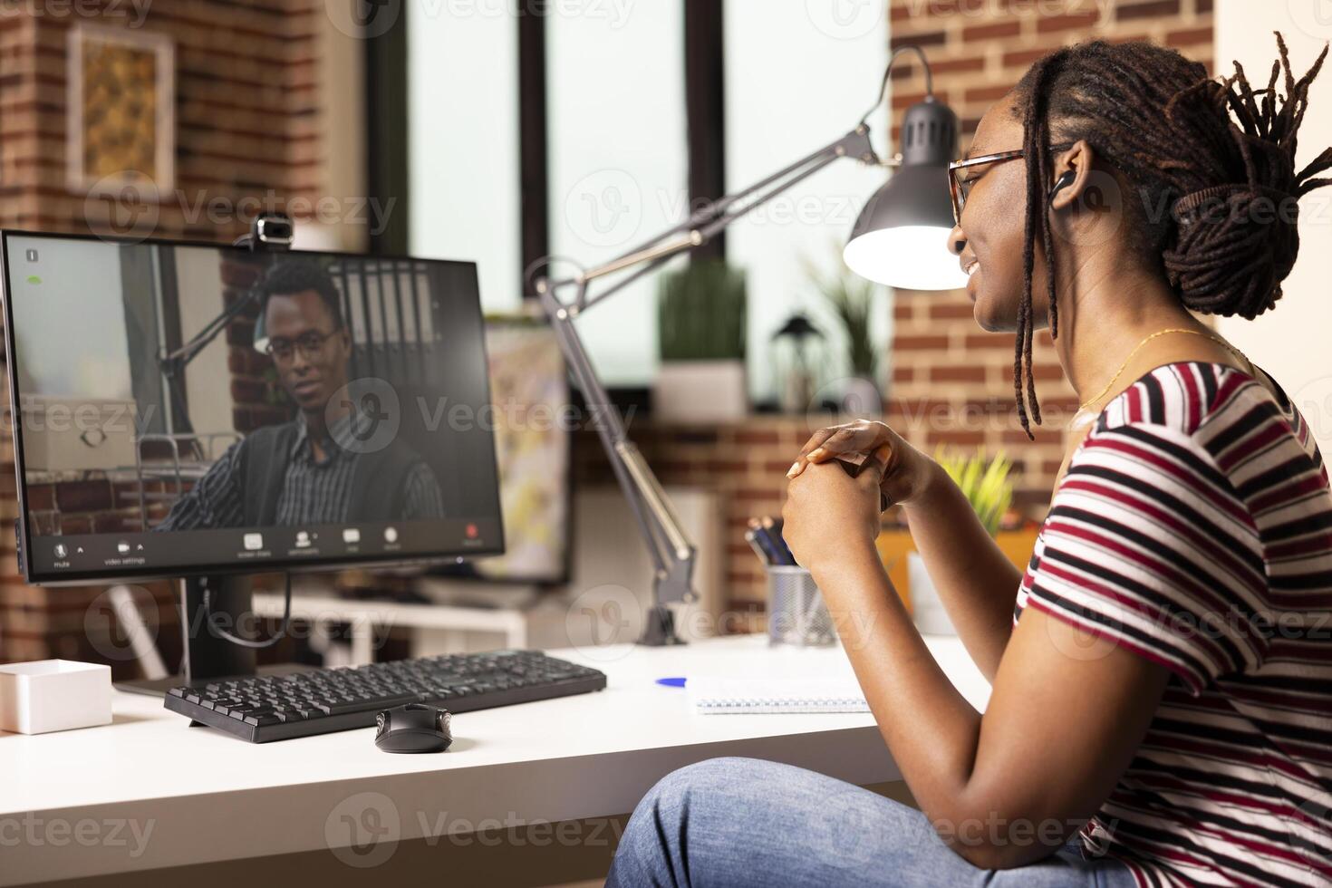 Smiling black woman seated at desk, participates in virtual meeting with potential client. African american female employee working from home, having online discussion with male manager on call. photo