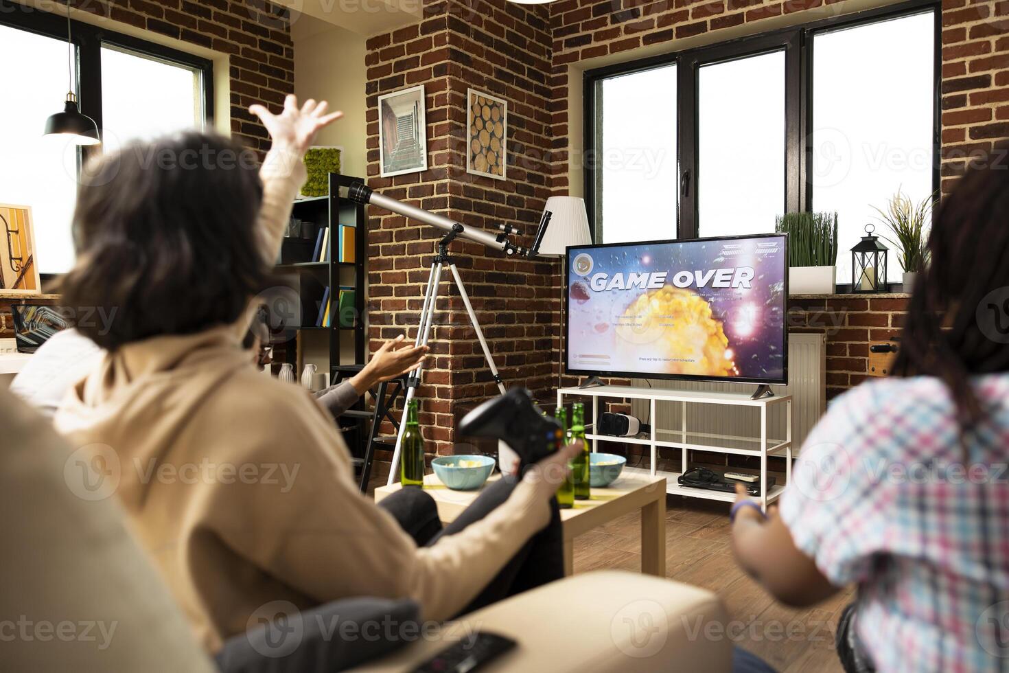 Caucasian woman holding wireless controller and reacting to game loss. Multiethnic group of friends playing games at home, as female individual throws her hands up in defeat. photo