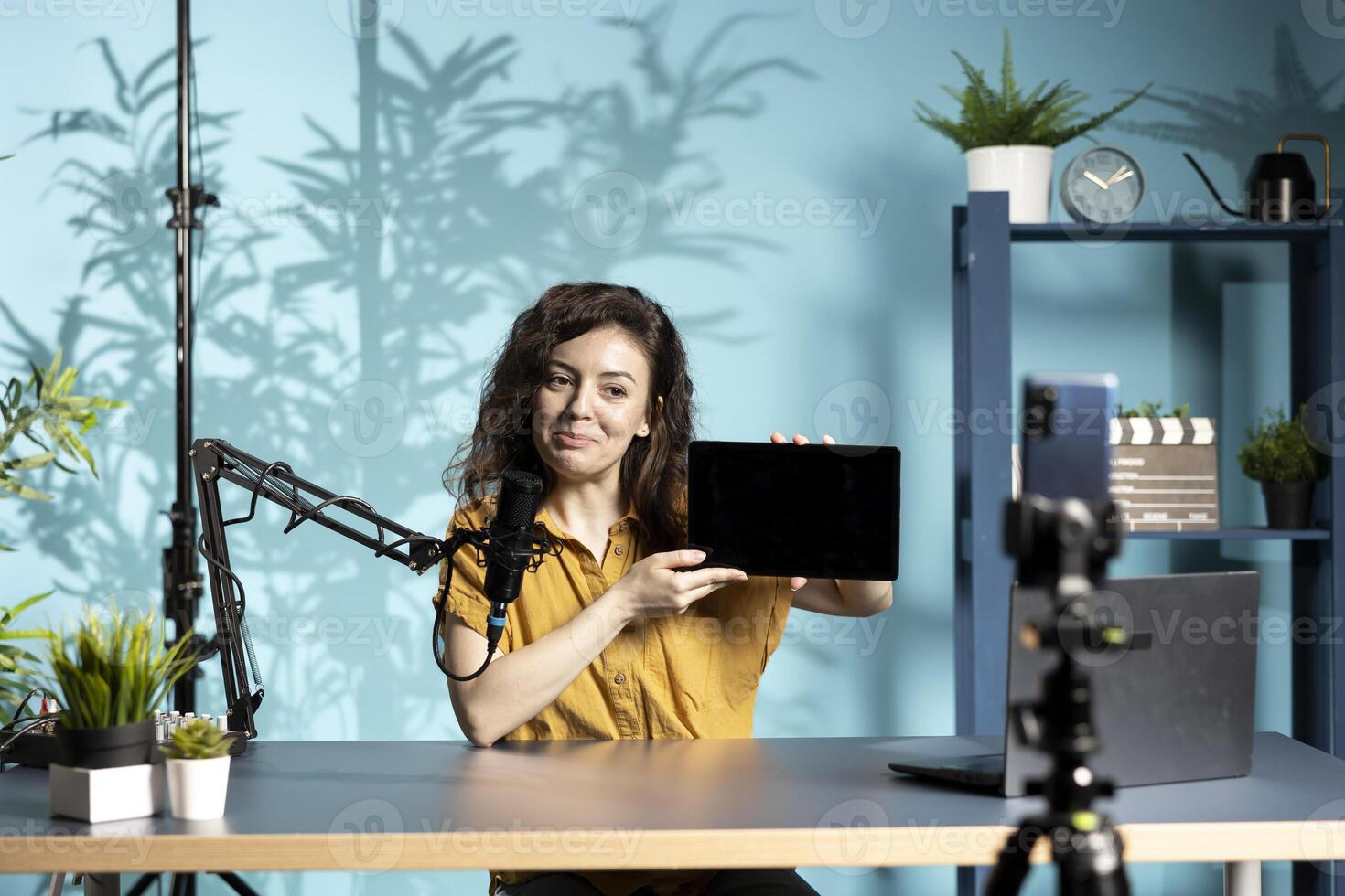 Happy tech expert presenting tablet, filming with smartphone camera. Joyful tech content creator reviewing digital device in front of online audience, recording with phone photo