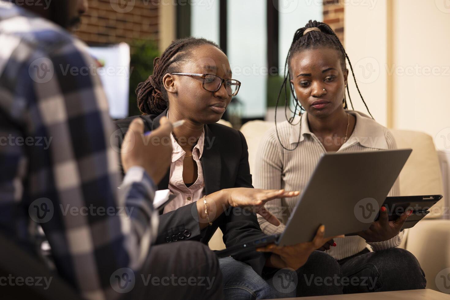 African American startup team work together in reviewing documents and digital report on laptop during financial project discussion. Professional woman explains marketing strategy plans to colleagues. photo
