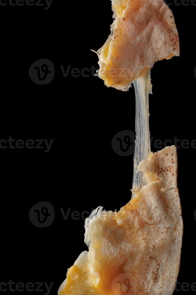 Melted kashkaval cheese stretching between two pieces of flatbread on dark background photo