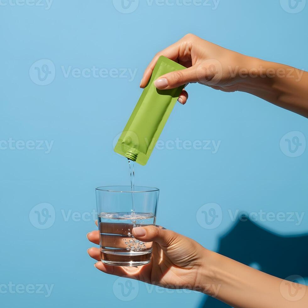 Green packet being poured into glass of water against blue background, Creating a refreshing hydration moment with a convenient green packet drink photo