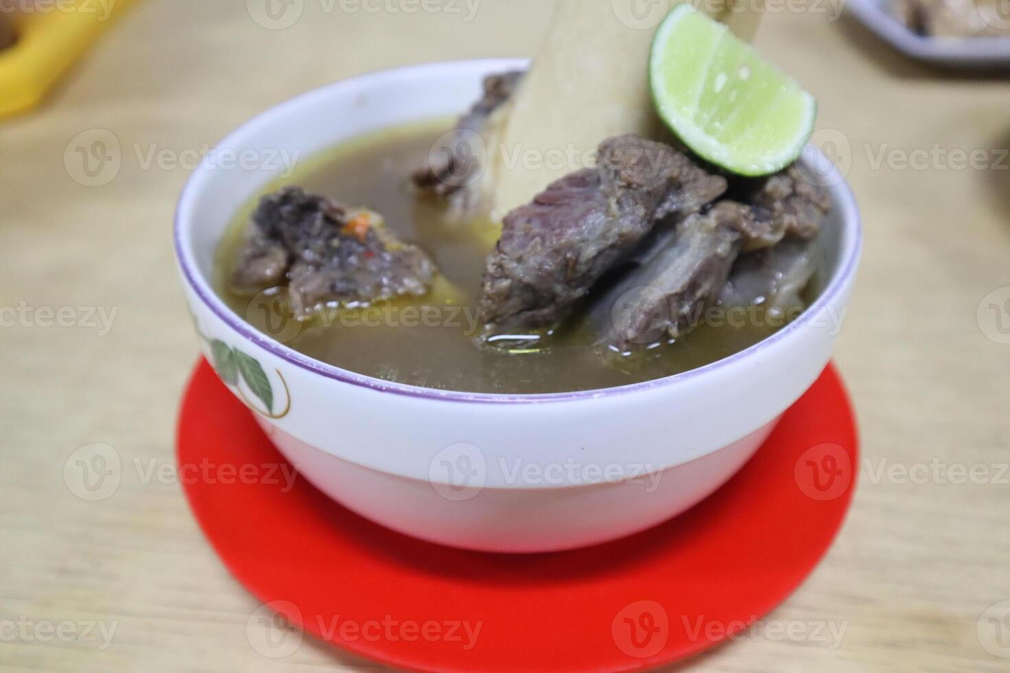 A bowl of soup with meat and lime on a red plate photo