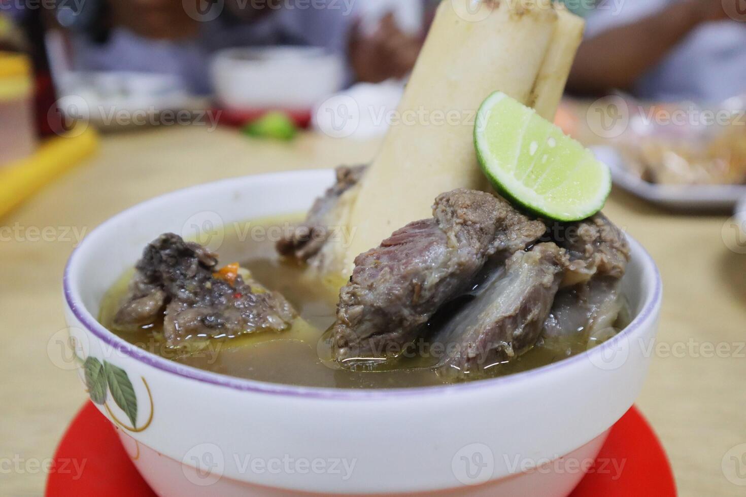 A bowl of soup with meat and a lime wedge photo
