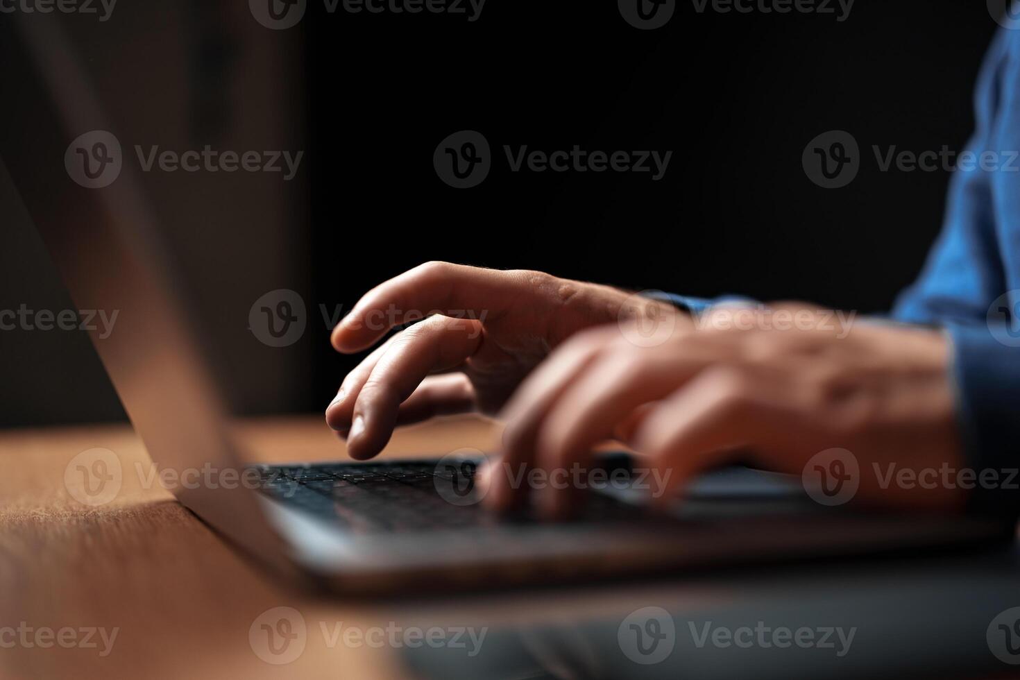 Hands typing on a laptop in a dimly lit room during the evening hours photo
