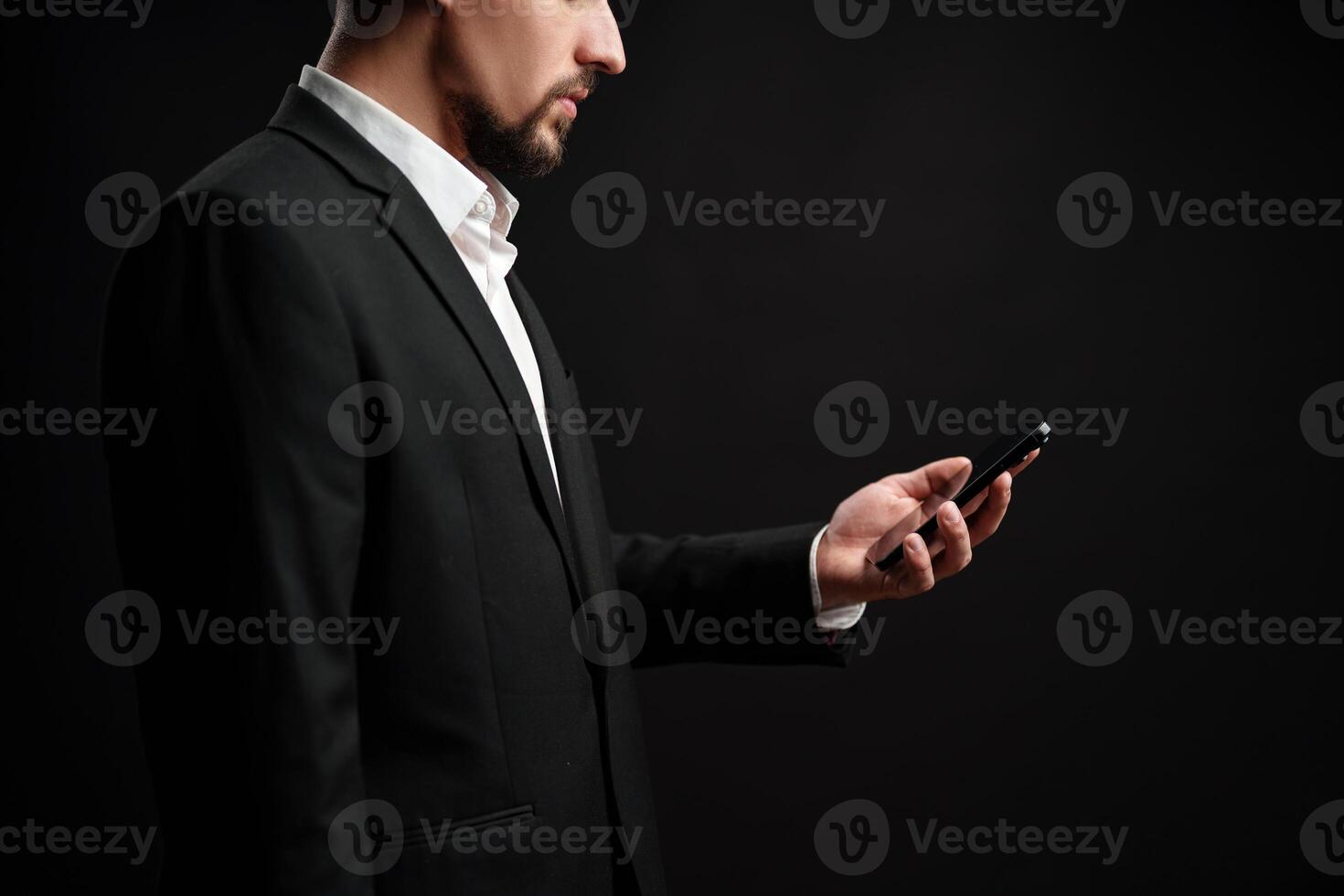 Professional man checking his smartphone while dressed in formal attire against a dark background photo