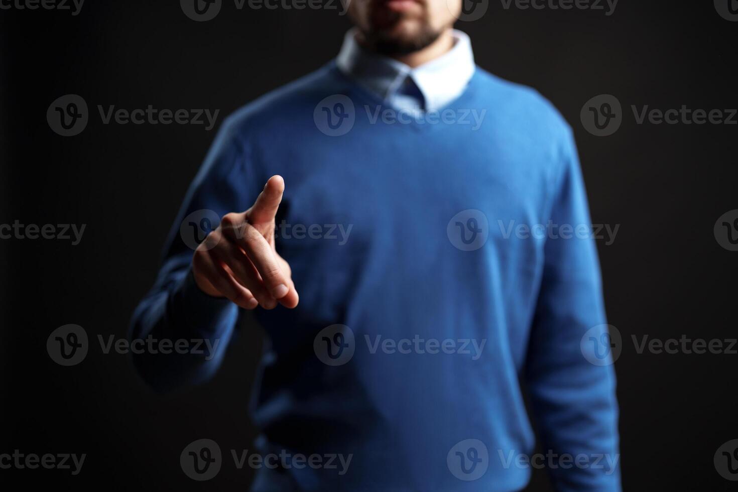 Man in blue sweater gestures confidently with a pointed finger against a dark background photo