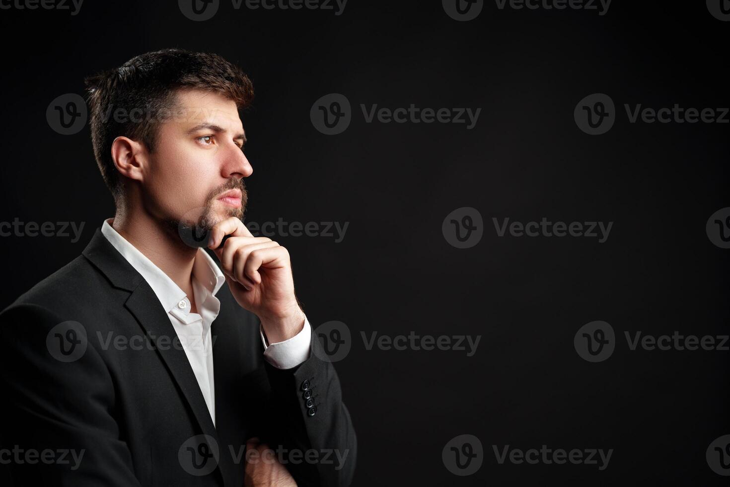 Man in a business suit contemplating ideas against a dark background in a studio setting photo