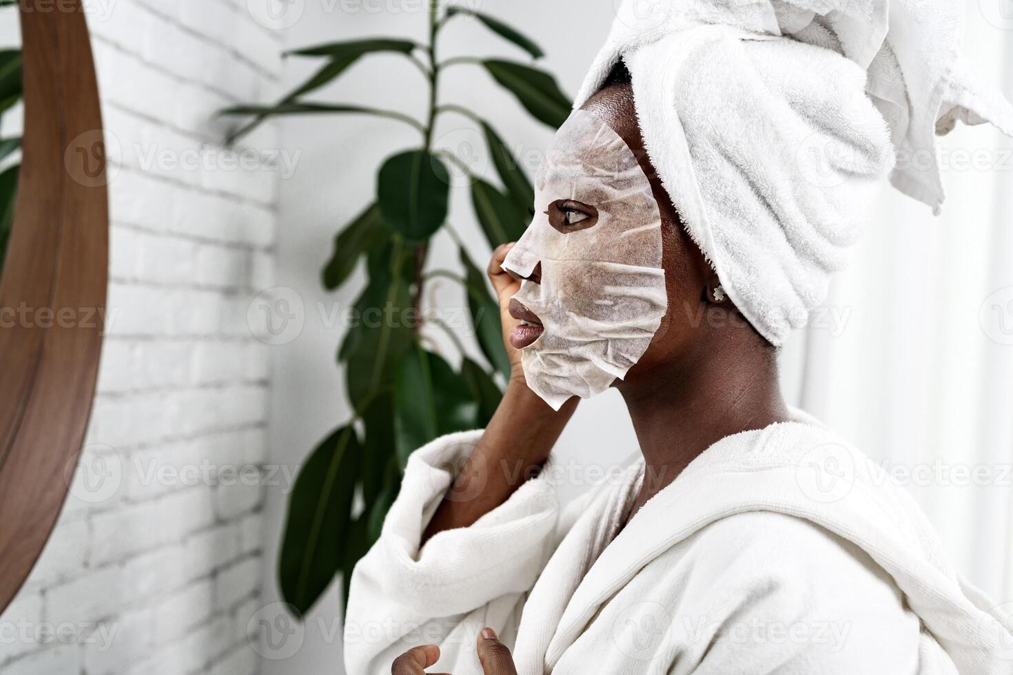 Woman applying a face mask while looking in the mirror at home spa setting during morning routine photo