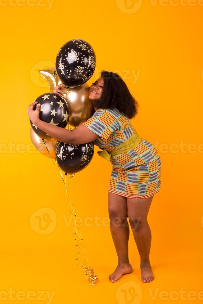 Holidays, birthday party and fun concept. Portrait of smiling young African-American young woman looking sweet on yellow background holding balloons. photo