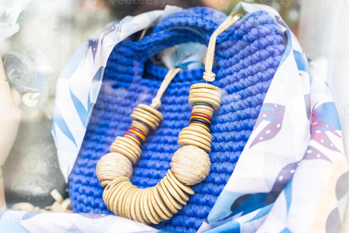 Colorful wooden necklace displayed on blue knitted bag. Handmade fashion, summer accessories, and artisan style in boutique showcase. photo