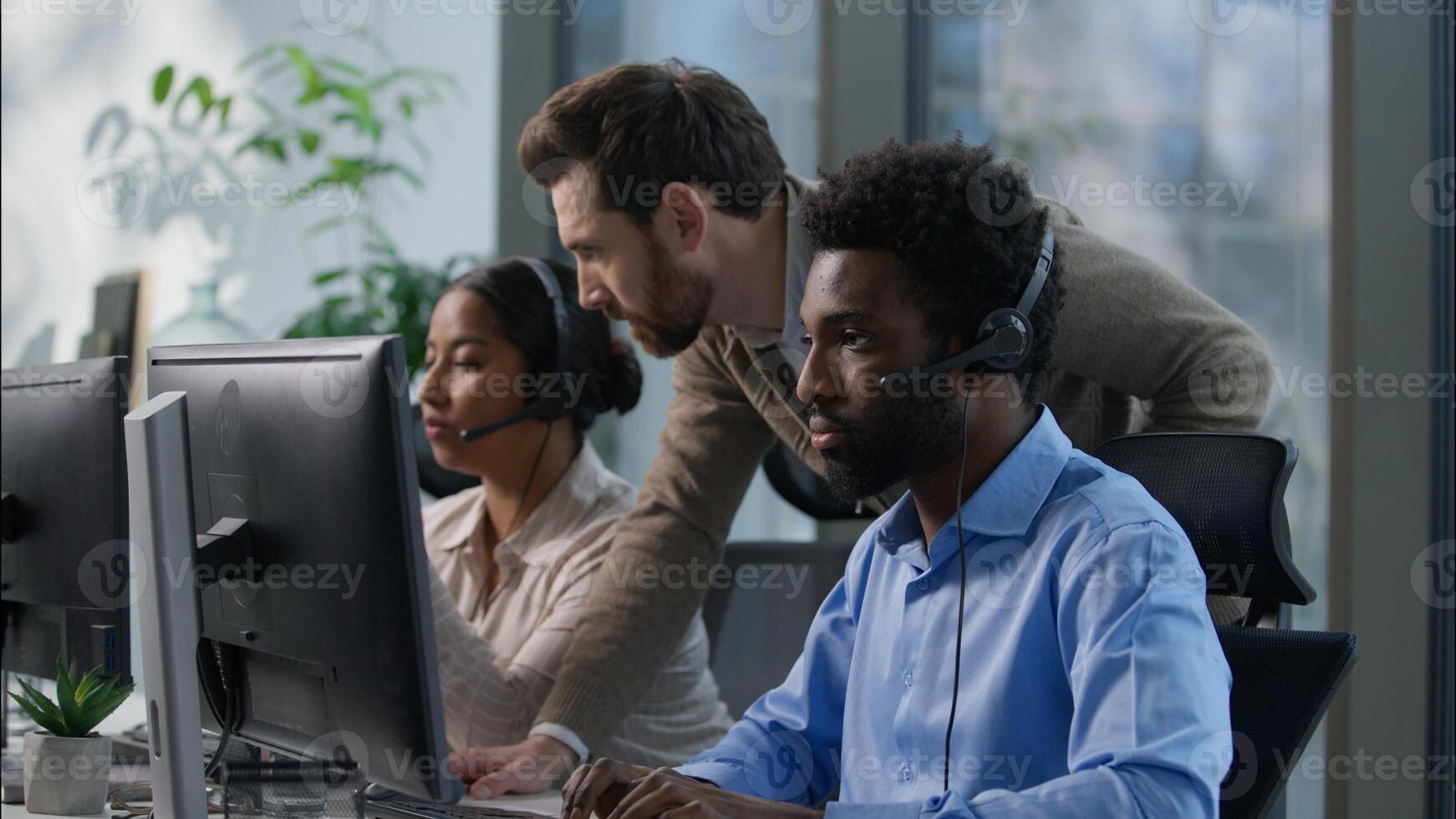 Callcenter teamwork multicultural office operators support communication African man Indian woman headset computer helpdesk Caucasian supervisor pointing monitor giving instructions customer service photo
