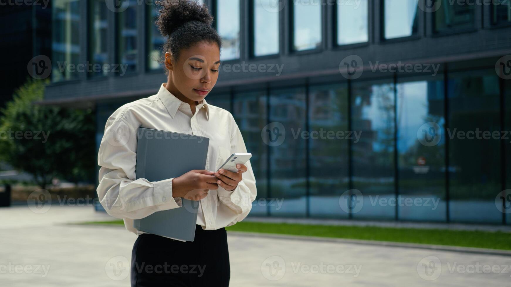 Addicted African American businesswoman business woman girl manager female using mobile phone walking in city working chatting with smartphone online internet scrolling going to office check message photo