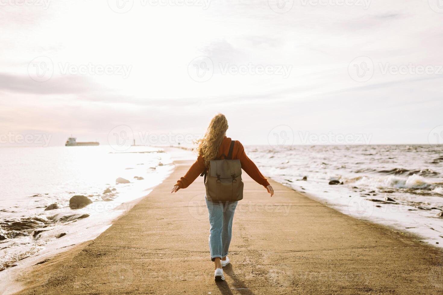 Woman enjoying breezy day near vibrant red lighthouse at sunset time Travel, weekend, lifestyle concept. photo