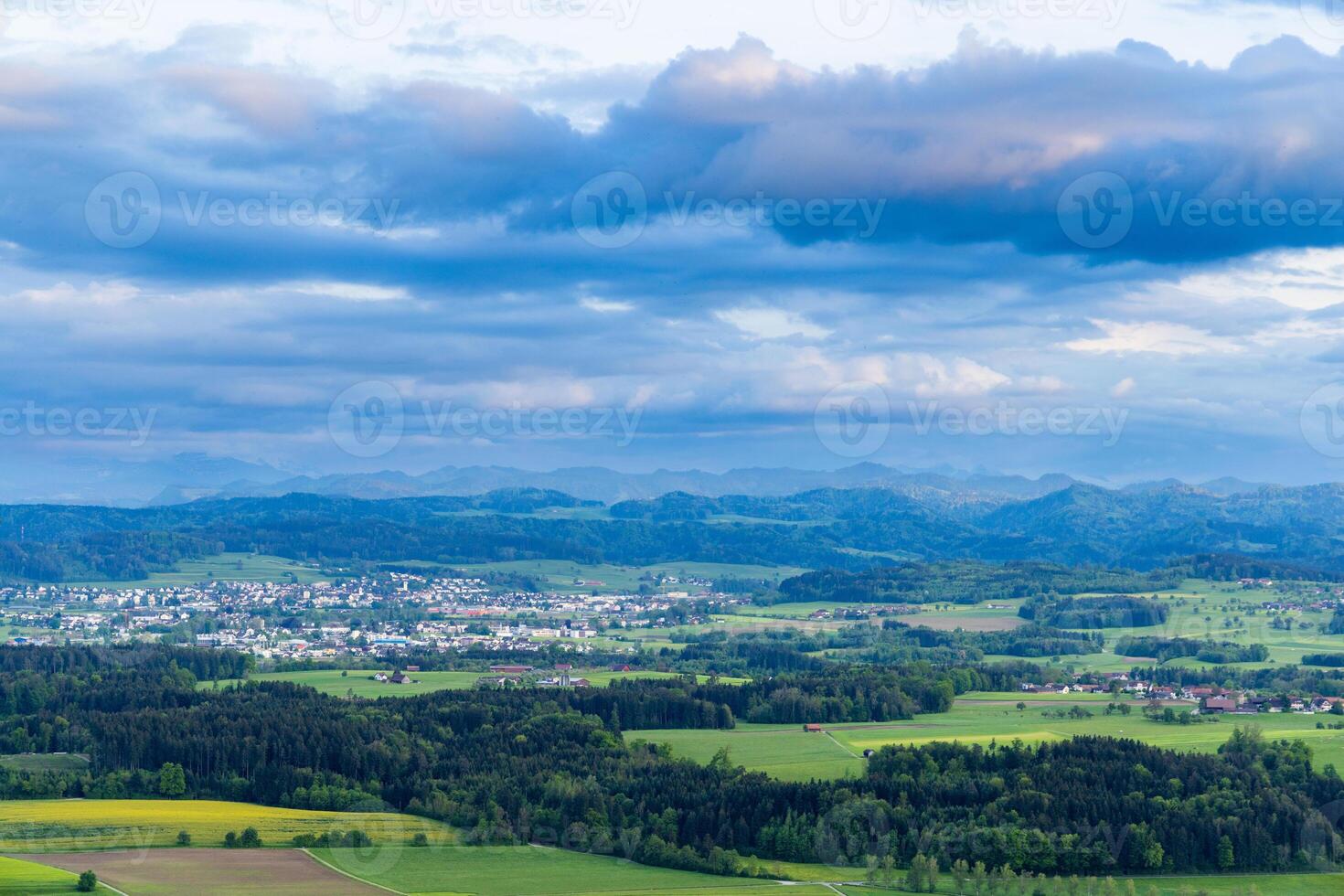 View of a forest, fields and village on the hills against a cloudy sky photo
