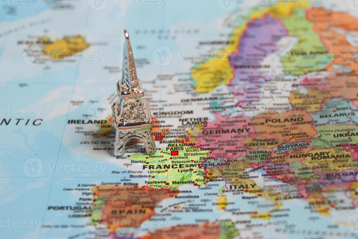Studio photo of a miniature silver Eiffel Tower positioned over France on a colorful world map, symbolizing travel plans, Paris dreams, and European journeys.