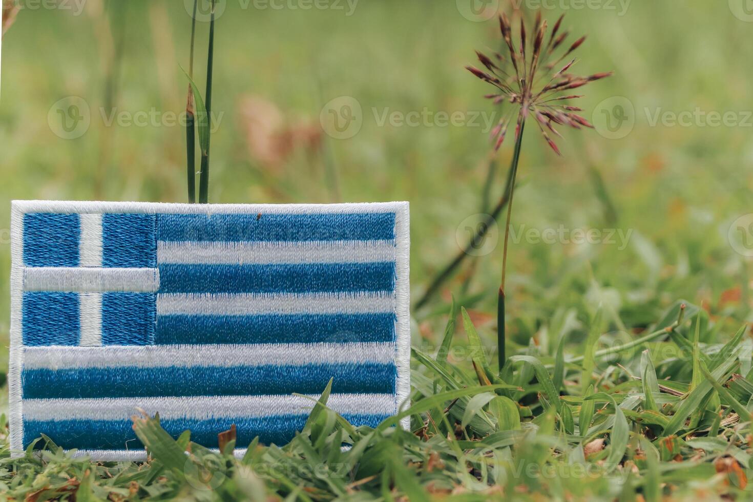 Eco friendly embroidered Greek flag lying on natural grass with wildflowers. Natural light, earth day, climate change theme. Horizontal photo with copy space.