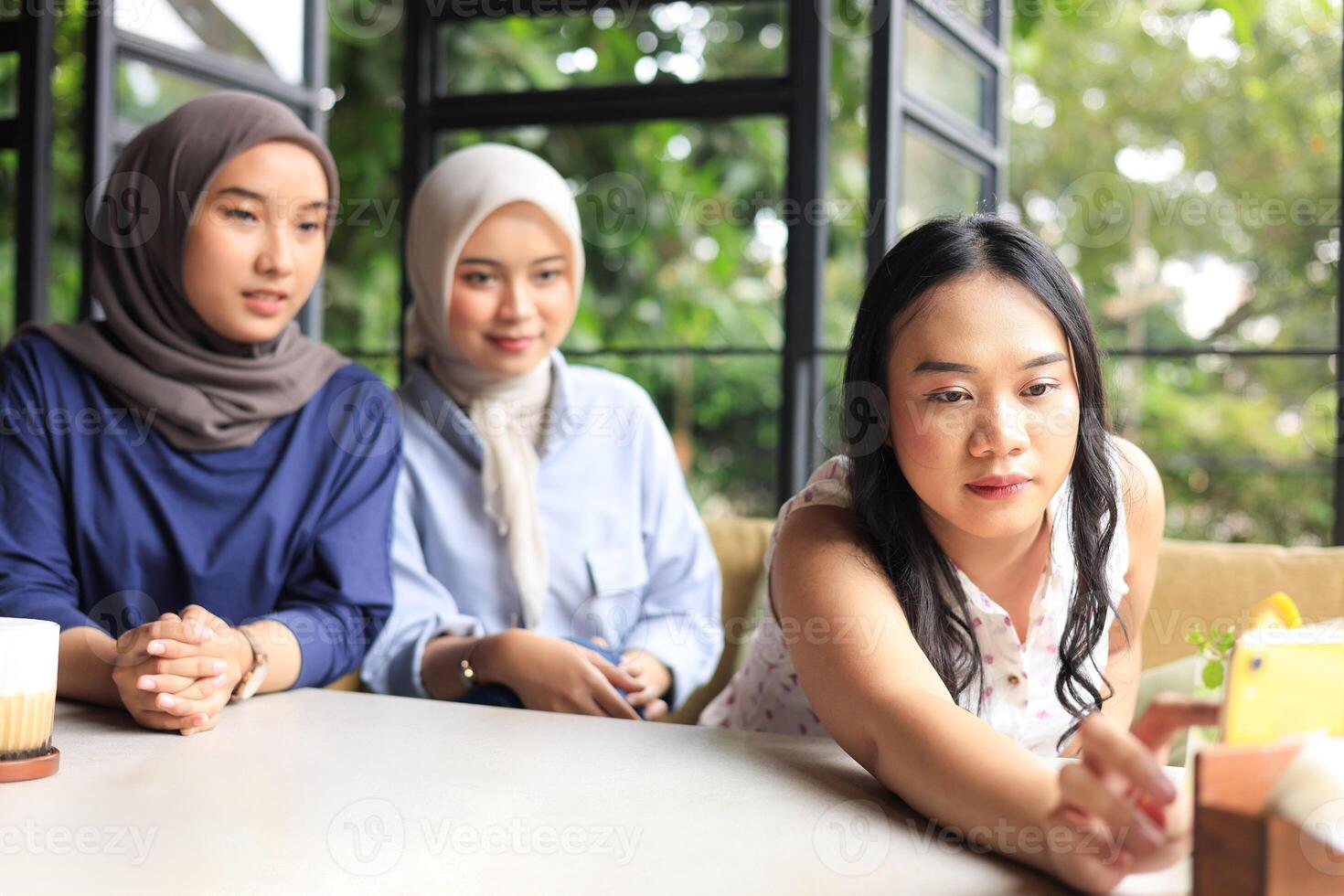 Three Asian Female Friends Happy Sitting in Cafe Next to Window doing Internet Trend Challenge photo