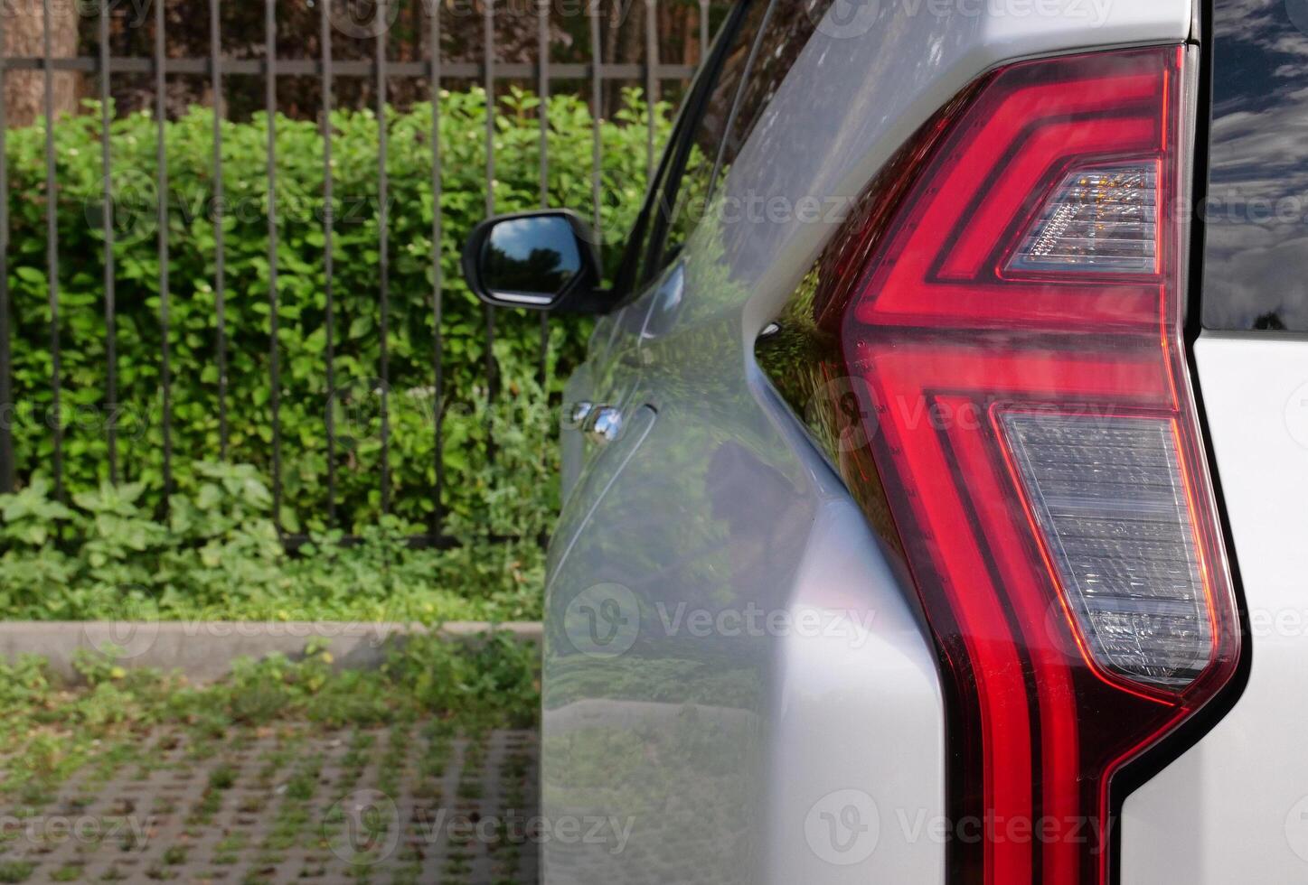 Rear LED Lights Of Large SUV With Fence And Green Hedge On Background photo