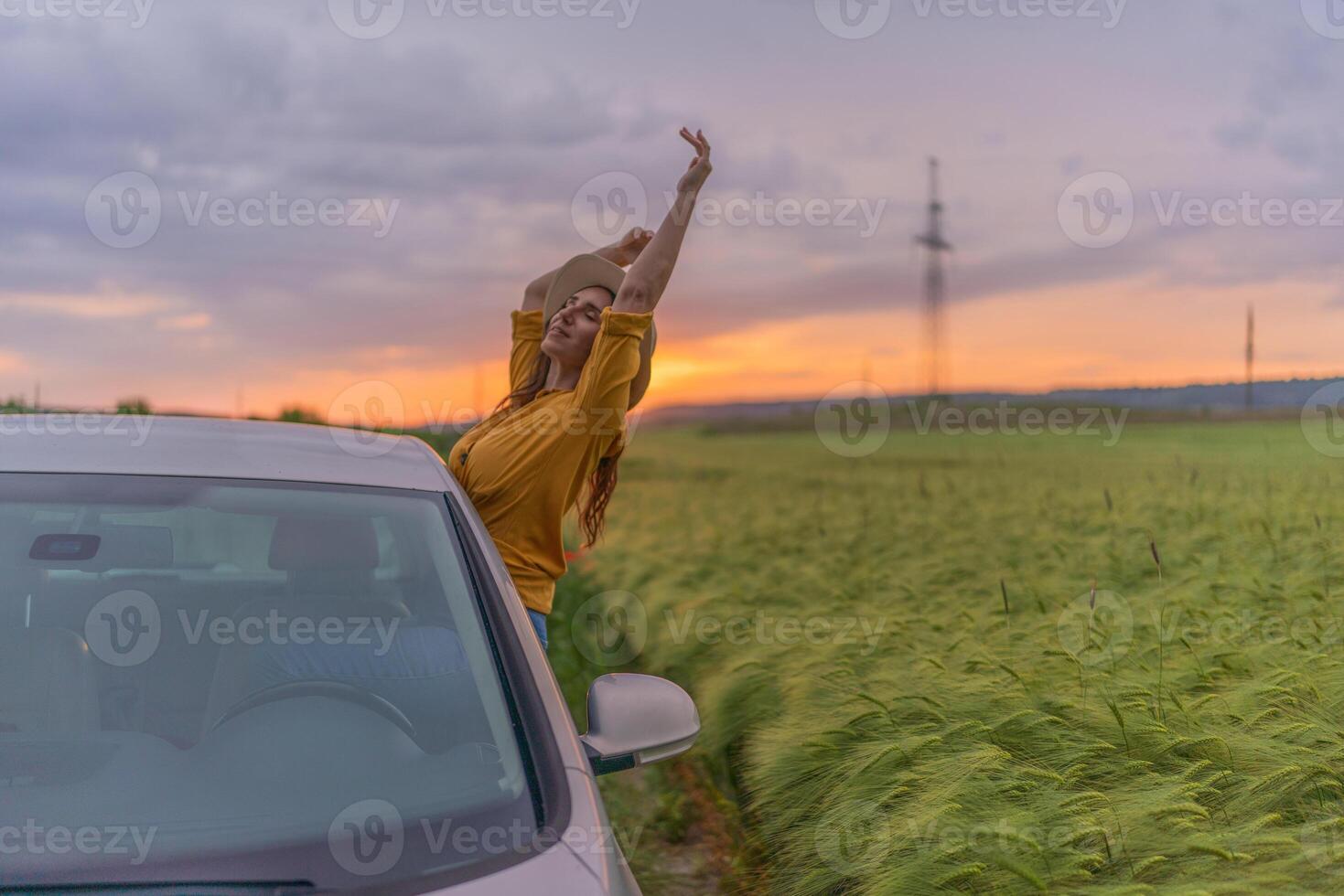 A woman is standing in a field with a car behind her photo