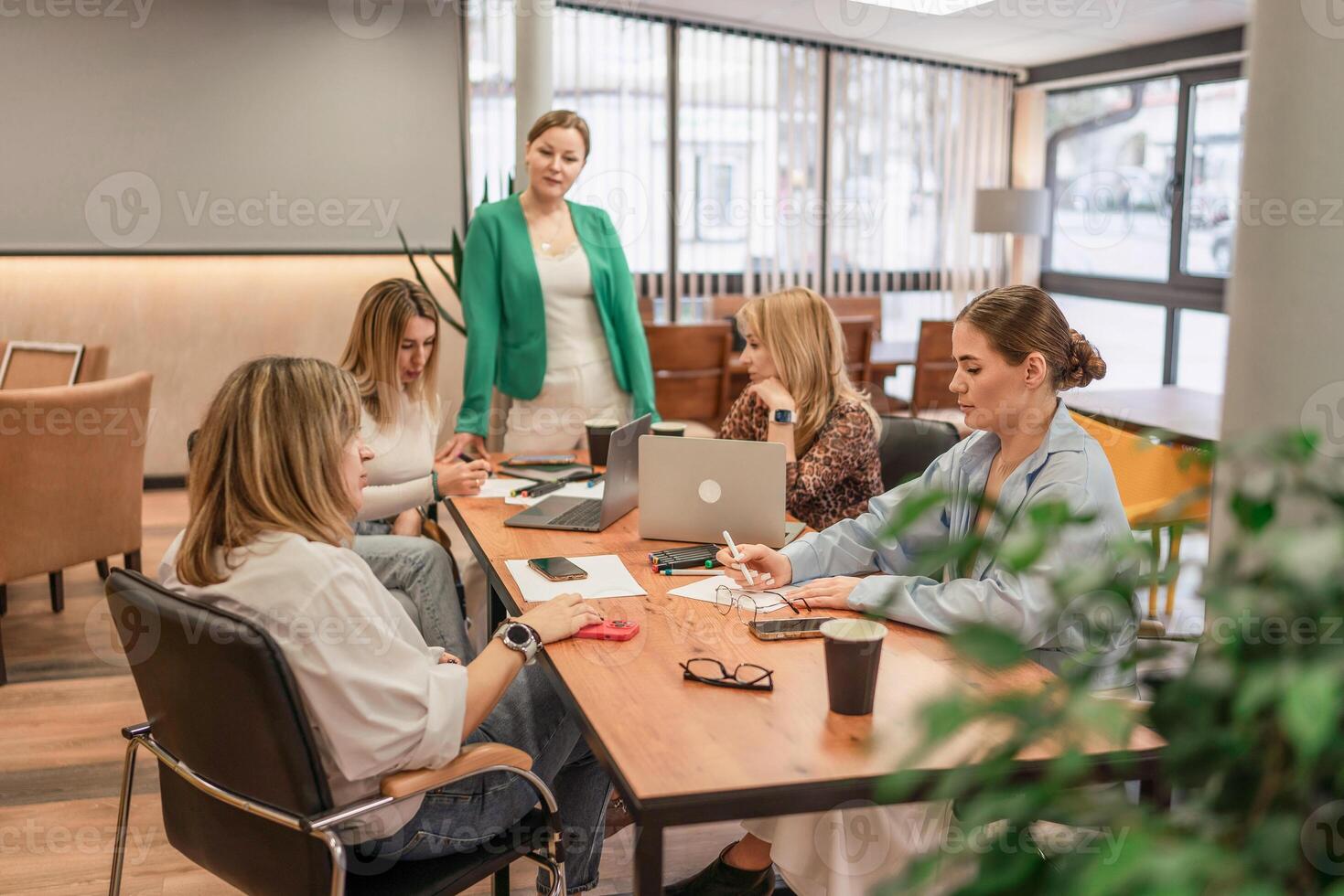 Businesswomen Meeting Laptops. Team brainstorms at office table, daytime, for project development discussion. photo