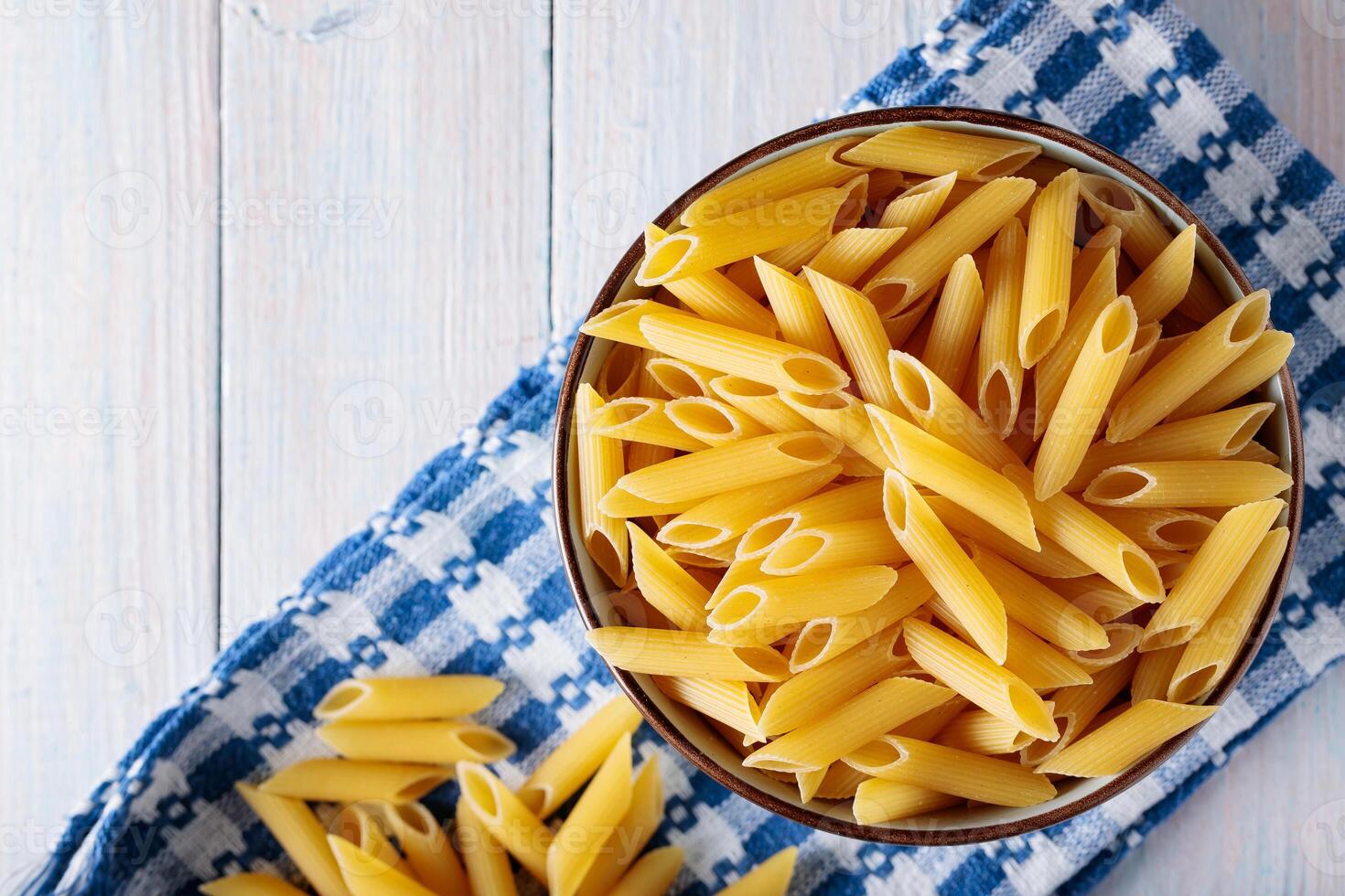 Penne Pasta in Bowl on Blue White Kitchen Towel Wooden Background photo