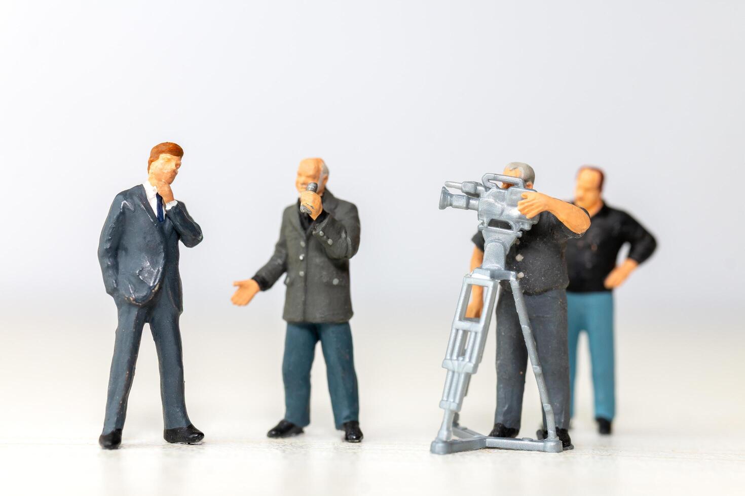 Miniature figure of a male journalist interviewing a businessman with a cameraman recording photo