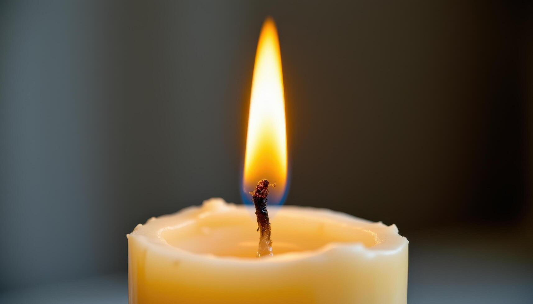 close up view of a flame climbing up the wick of a tall taper candle, surrounded by softly melting wax. photo