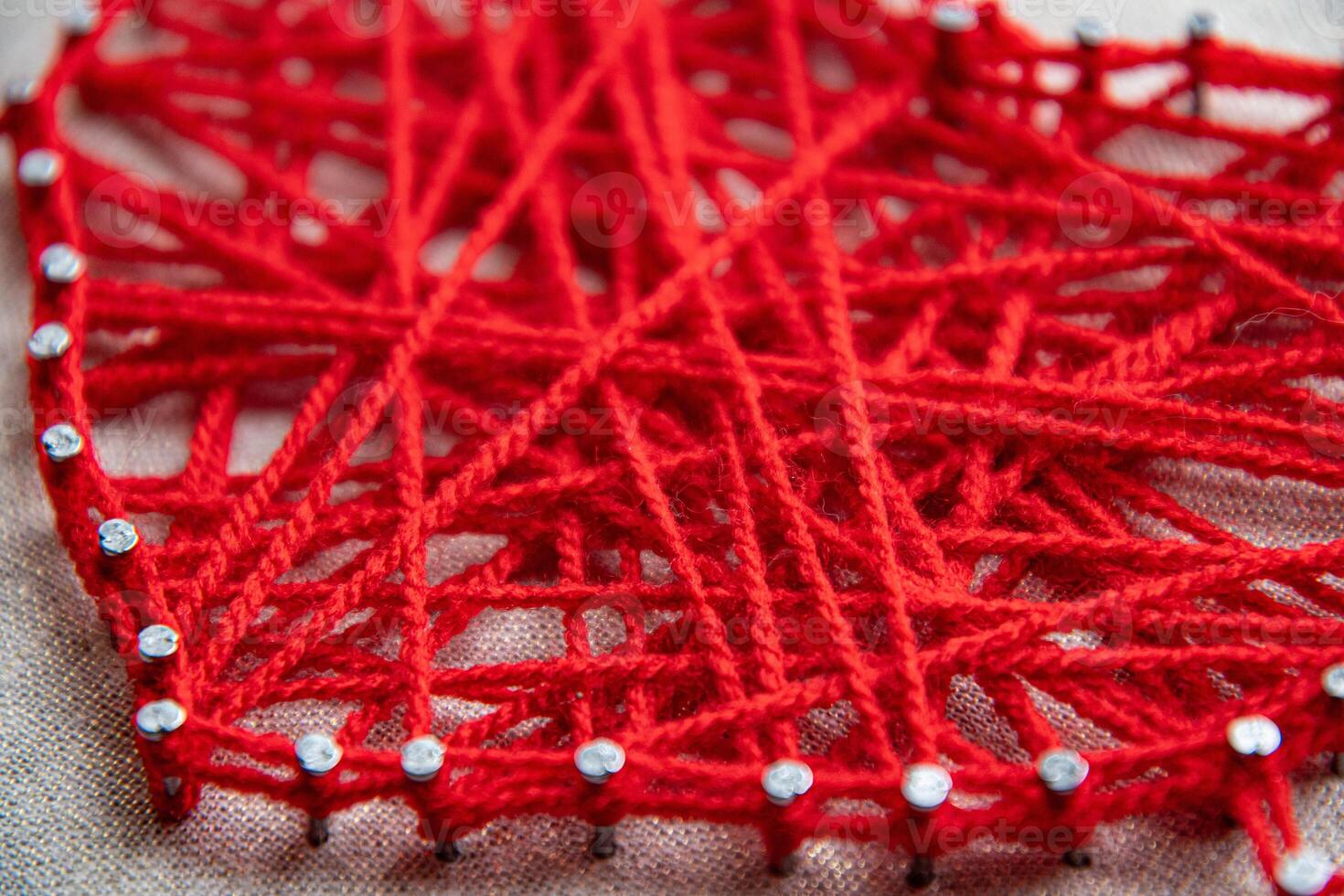 Creative use of vibrant red yarn intertwined around nails forms string art, showcasing textures and patterns. Techniques highlight craftsmanship and artistic expression. photo