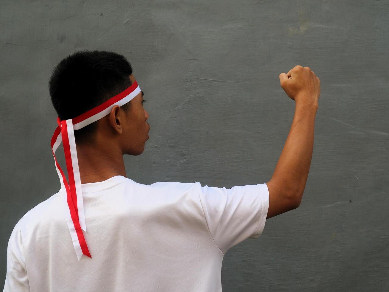 Indonesia young man wearing red white headband and clenched fist against grey background photo