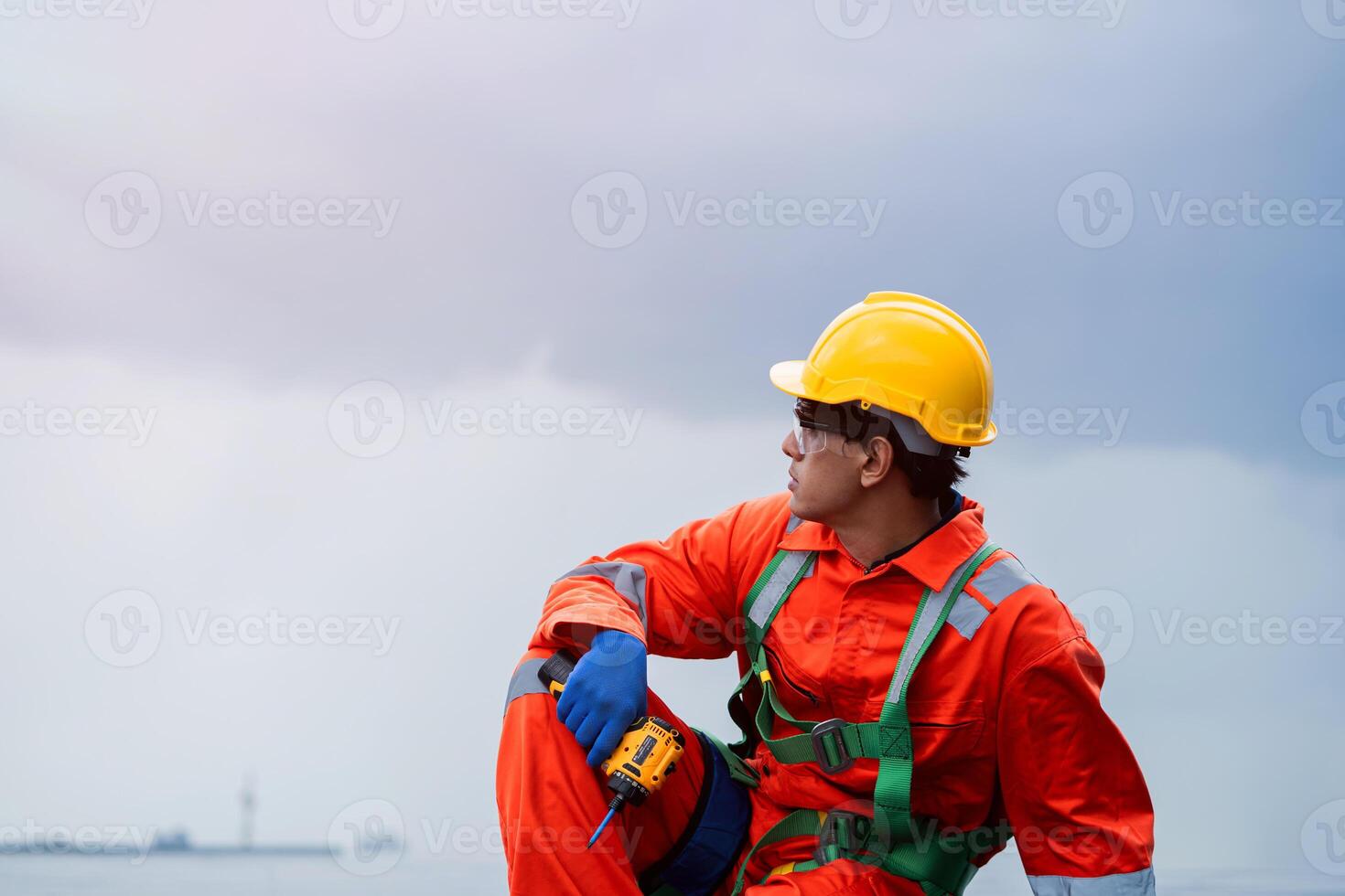 A man in a yellow helmet and orange jumpsuit is sitting on the ground photo