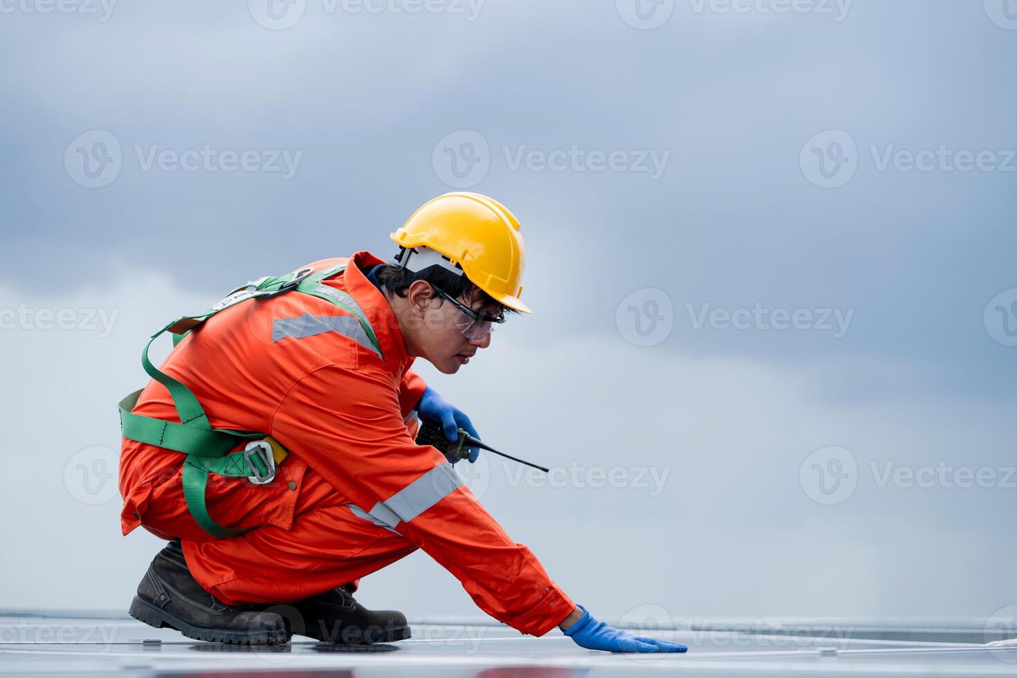 A man in an orange jumpsuit is crouching on a roof photo