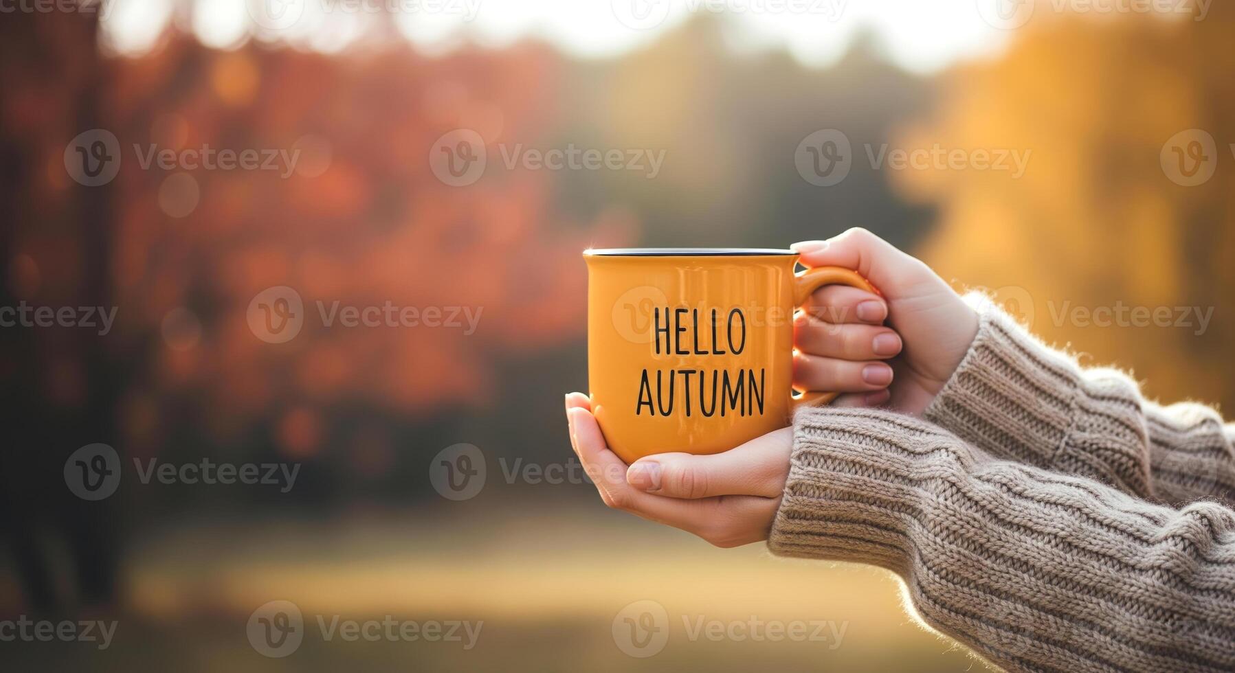 Hands hold an orange mug with Hello Autumn text amidst fall foliage. Cozy season, warm drinks, and nature. photo