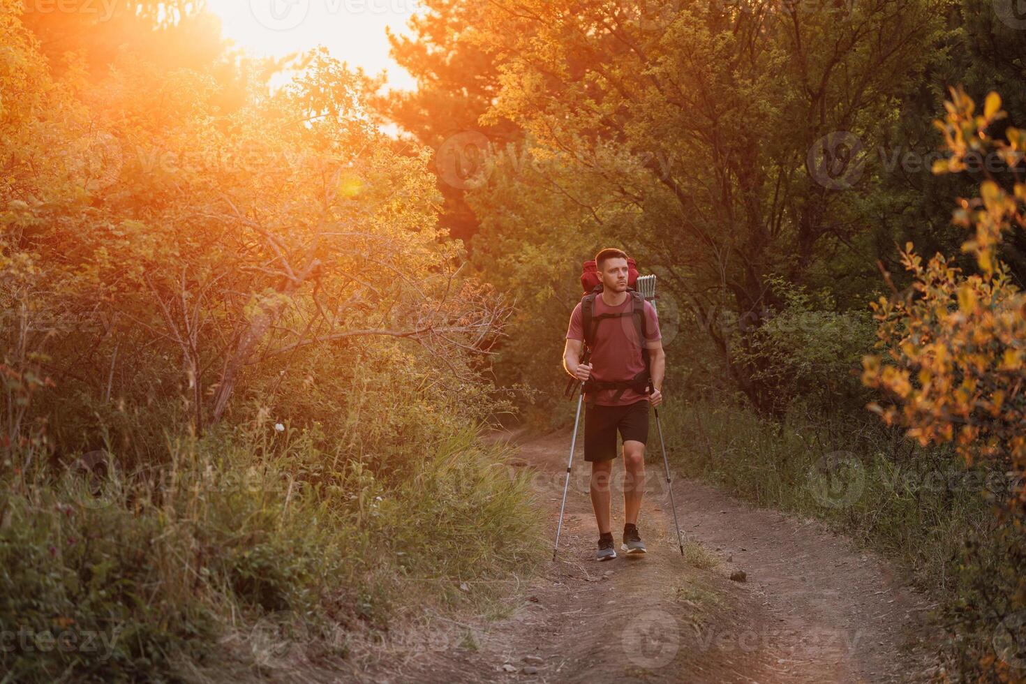 Hiker trekking through forest path with backpack and poles at warm sunset. Active lifestyle and adventure hiking concept. photo