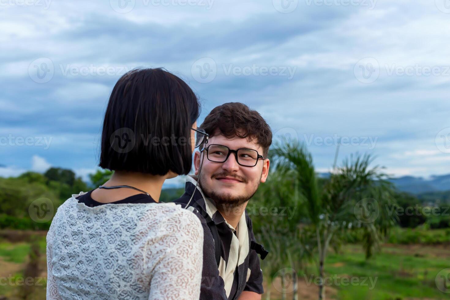 Man and woman at sunset in mountains. Young couple sharing joyful moment outdoors, surrounded by vibrant greenery and cloudy sky, capturing the essence of connection and happiness in natural setting photo