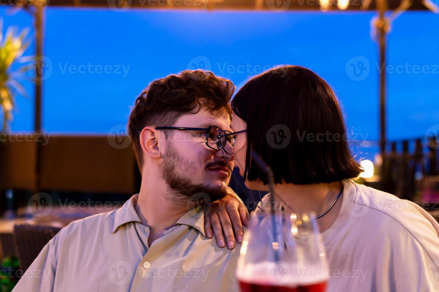 Romantic date on restaurant terrace at sunset. Romantic couple enjoying tender moment together at sunset, surrounded by cozy outdoor atmosphere, with drinks and evening sky creating warm ambiance photo