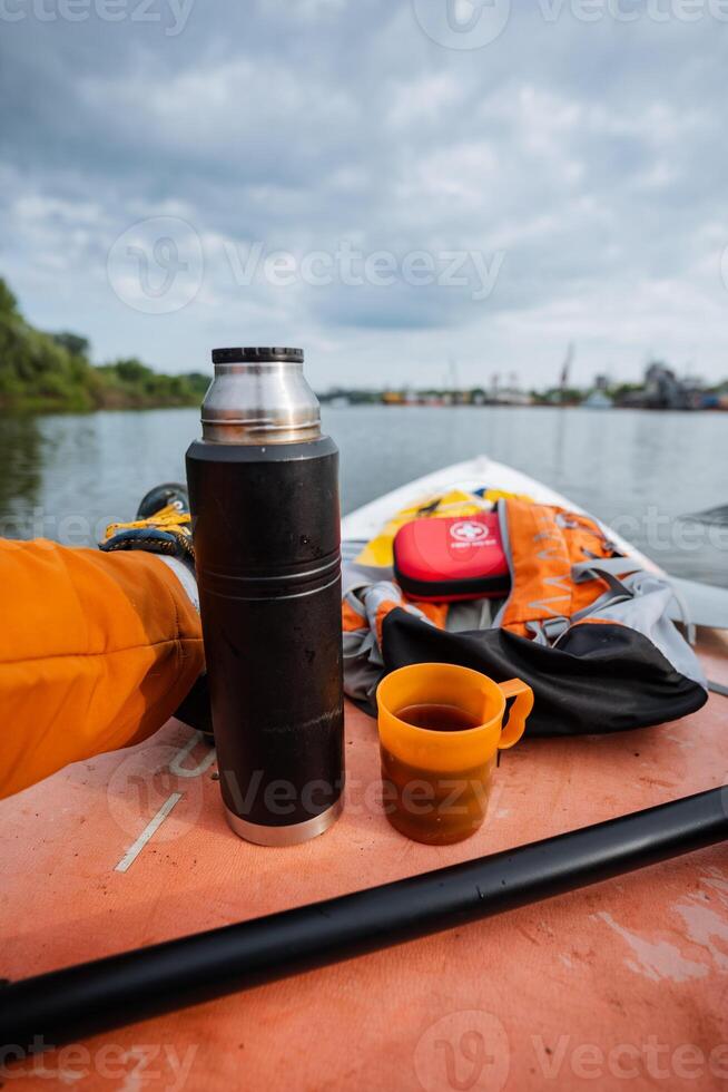 A person is comfortably sitting in a small boat, enjoying the serene surroundings, with a thermos filled with hot coffee and a cup ready to sip from. Its a peaceful moment on the water photo