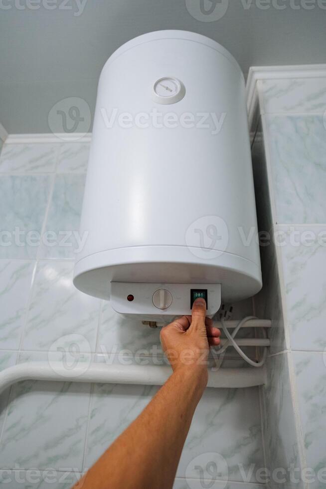 In a bathroom, an individual is deliberately pressing a button on a water heater, which is specifically designed to heat water for various purposes such as bathing, cleaning, and cooking photo