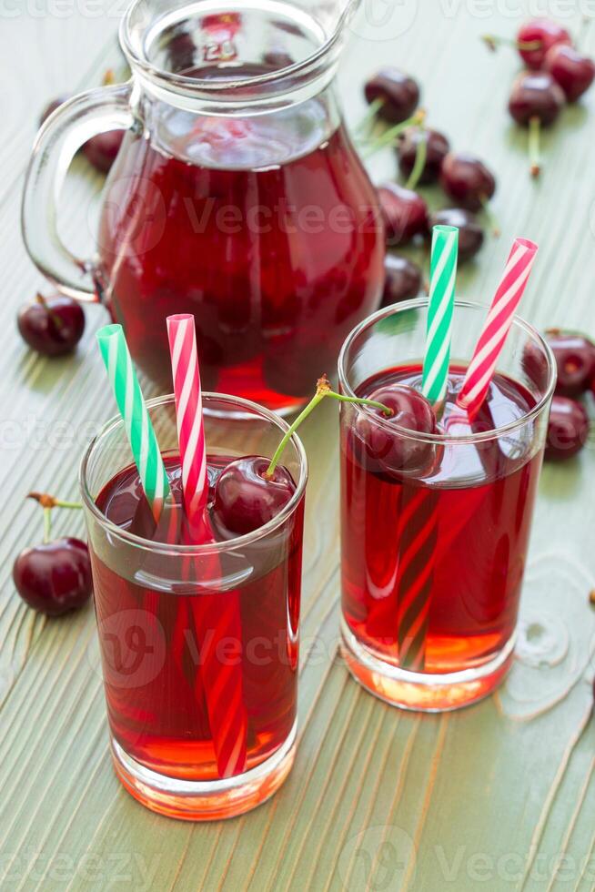 Two glasses of cherry juice with straws in foreground and in the background a jar full of cherry juice. 2 cherry juices. Vertical. Close-up. Daylight. photo