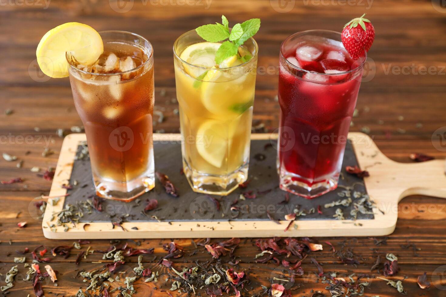 Three tall glasses of iced drinks placed on a wooden tray feature bright colors and fresh garnishes. Ideal for warm days, these refreshments showcase a variety of flavors and ingredients. photo