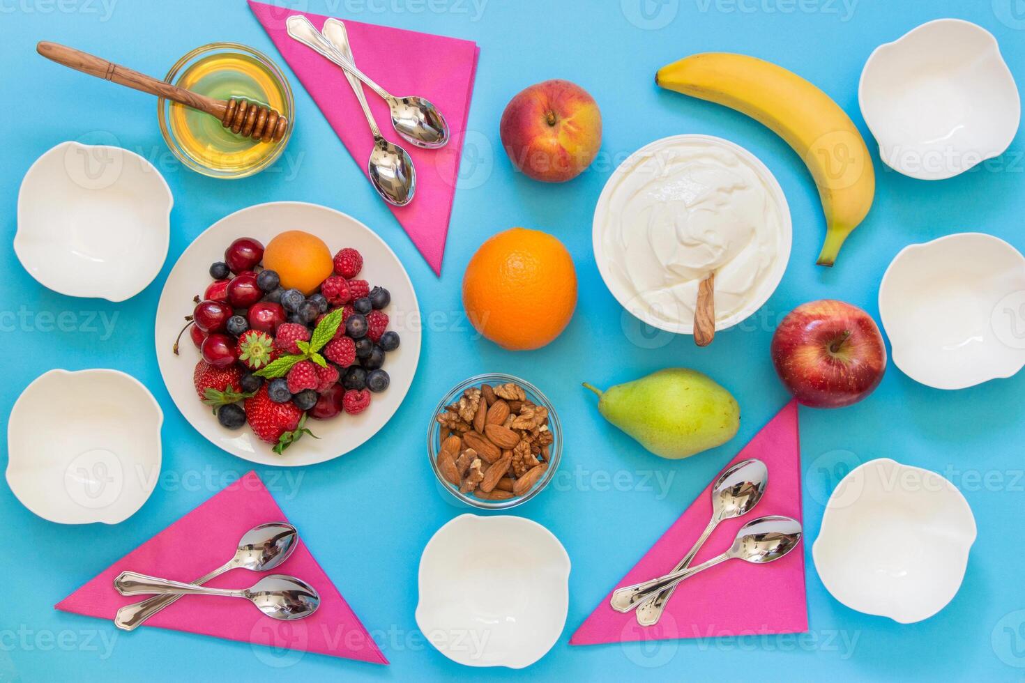 Greek yogurt around a variety of fruits and berries, nuts, honey and 6 empty bowls, 6 spoons and napkins on a light blue background. Yogurt and a variety of ingredients for it. Horizontal. Top view. photo